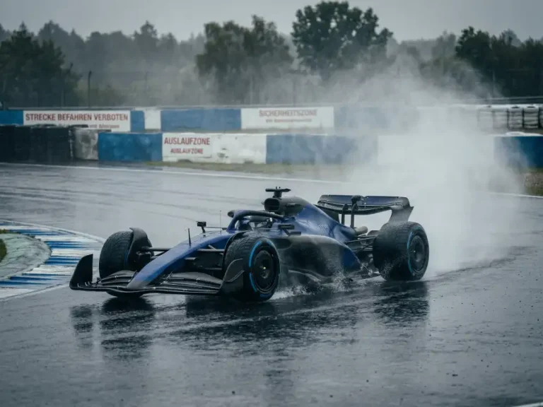 Formel-1-Bolide mit Regenreifen und hoher Wassergischt auf nasser Rennstrecke bei starkem Regen